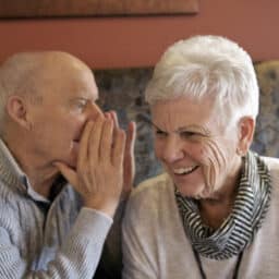 Senior man talking in his friends ear so she can hear