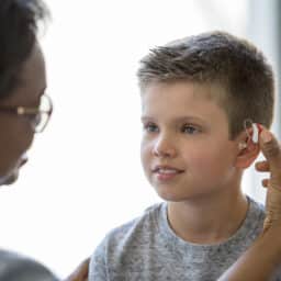 Young child and his mom get ready for school by putting in his hearing aid.