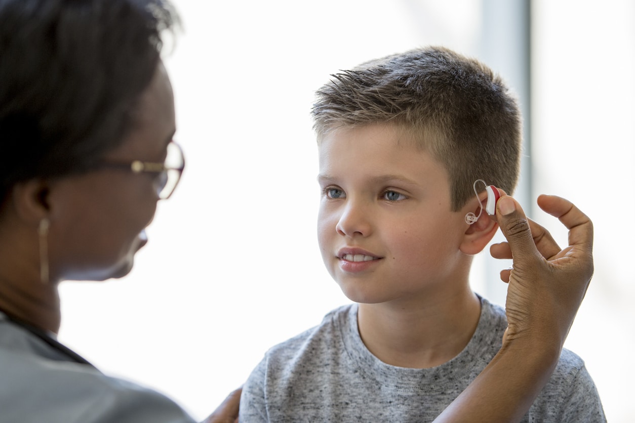Young child and his mom get ready for school by putting in his hearing aid.