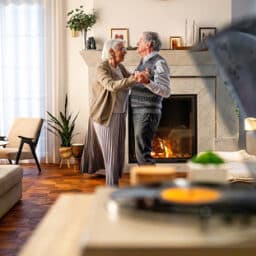 Happy older couple dancing to their record player in their living room.