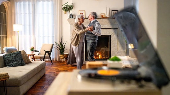 Happy older couple dancing to their record player in their living room.