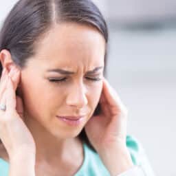 Woman with tinnitus looking distressed and holding her ears.