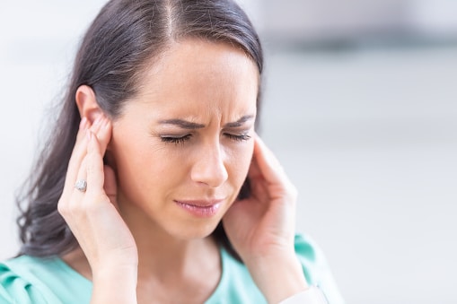 Woman with tinnitus looking distressed and holding her ears.