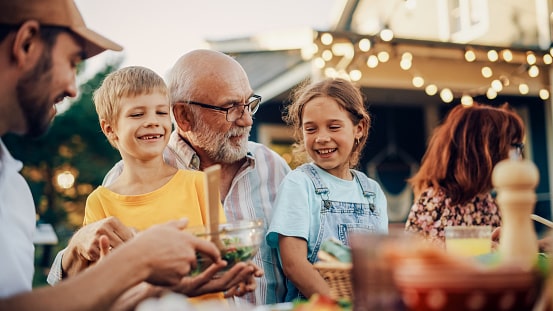 Happy family enjoying an outdoor barbecue on a pleasant summer evening. Grandfather and his grandchildren having summer fun.
