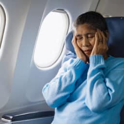 Woman with tinnitus holds her head and feels uncomfortable during a flight.