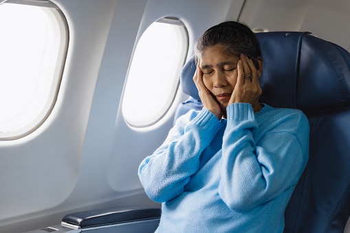 Woman with tinnitus holds her head and feels uncomfortable during a flight.